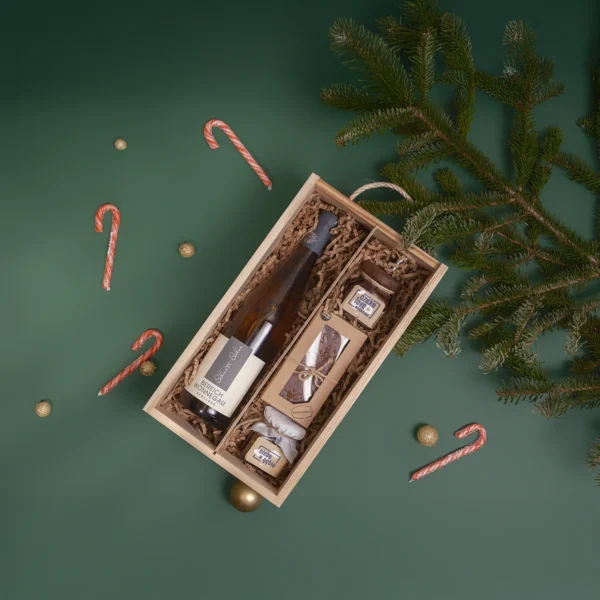 Zestaw prezentowy z białym winem w drewnianej skrzynce, z piernikiem i słodkościami w świątecznej aranżacji