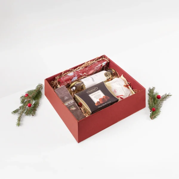 Czerwony zestaw prezentowy z winem, truflami i słodyczami w świątecznej aranżacji
