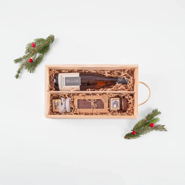 Zestaw prezentowy z białym winem w drewnianej skrzynce, z piernikiem i słodkościami w świątecznej aranżacji