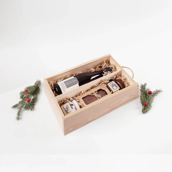 Zestaw prezentowy z białym winem w drewnianej skrzynce, z piernikiem i słodkościami w świątecznej aranżacji